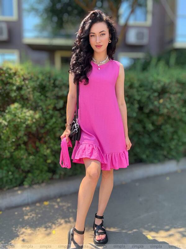 Woman in a pink dress standing outdoors with greenery in the background