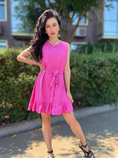 Woman in a pink dress standing outdoors with greenery in the background