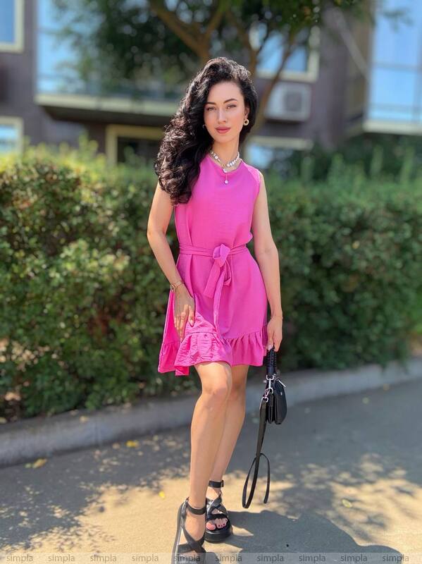 Woman in a pink dress standing outdoors with greenery in the background