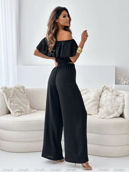 Woman wearing a black off-shoulder jumpsuit in a living room setting.