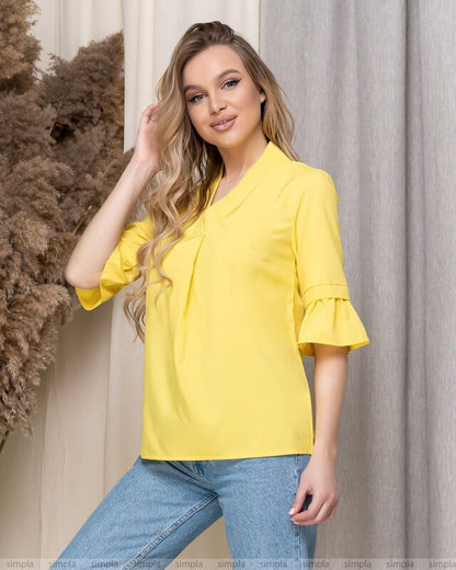 Woman wearing a yellow blouse with ruffled sleeves against a neutral background