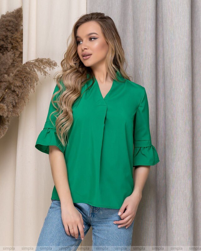 Woman wearing a green blouse with ruffled sleeves against a neutral background