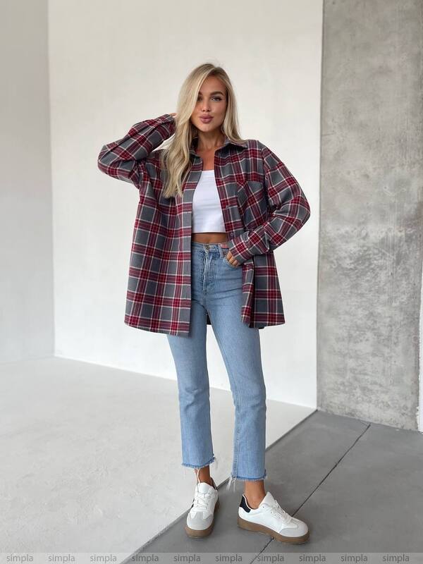 Woman wearing a plaid shirt, white top, blue jeans, and white sneakers against a plain background