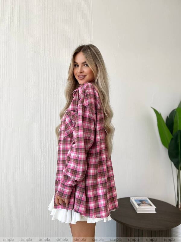 Woman wearing a pink plaid shirt with a white skirt in a room with a plant and table.