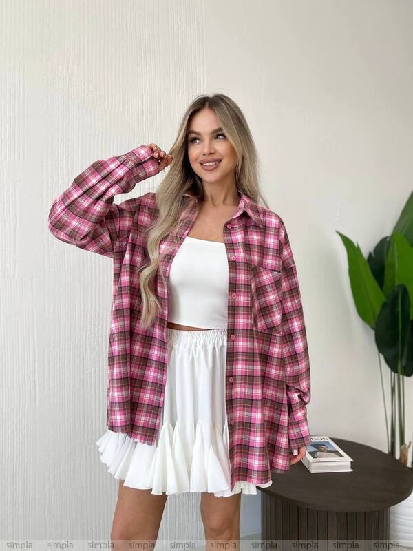 Woman wearing a pink plaid shirt over a white dress indoors.