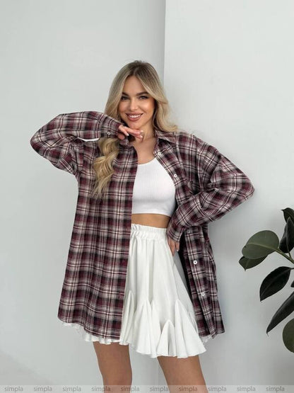 Woman wearing a plaid shirt over a white top and skirt against a white background