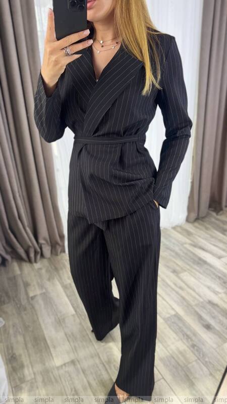 Woman wearing a black pinstripe suit in a room with curtains.