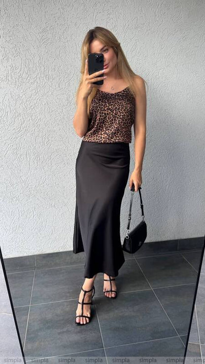 Woman taking a mirror selfie wearing a leopard print top and black skirt.