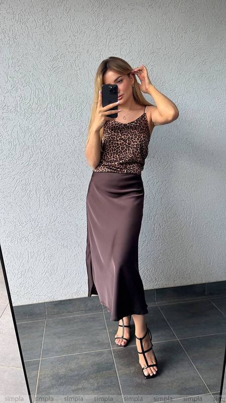 Woman taking a mirror selfie wearing a leopard print top and satin skirt.