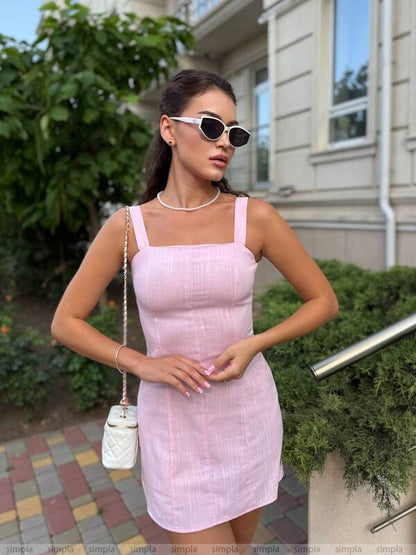 Woman in a pink dress standing outdoors with greenery and a building in the background