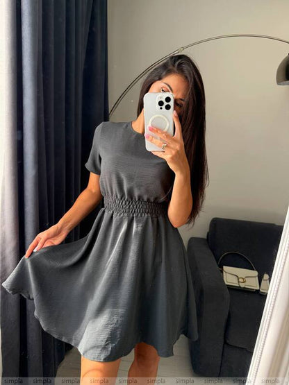 Woman taking a mirror selfie wearing a gray dress in a room with a couch and lamp.