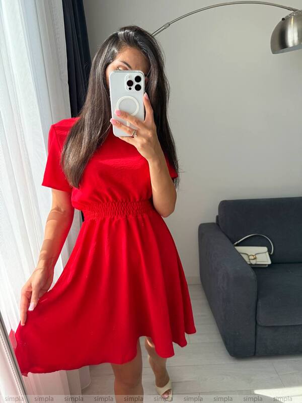 Person wearing a red dress taking a mirror selfie in a room with a gray sofa and white wall.