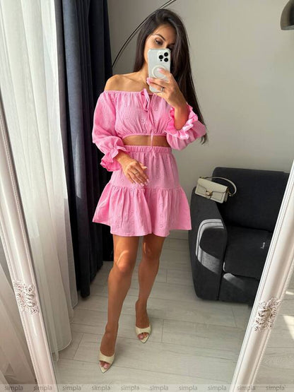 Woman wearing a pink off-shoulder top and skirt in a room with a gray sofa.