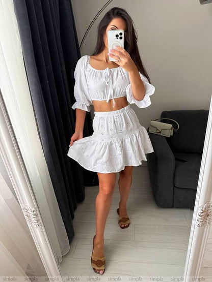 Woman taking a mirror selfie wearing a white outfit in a room.