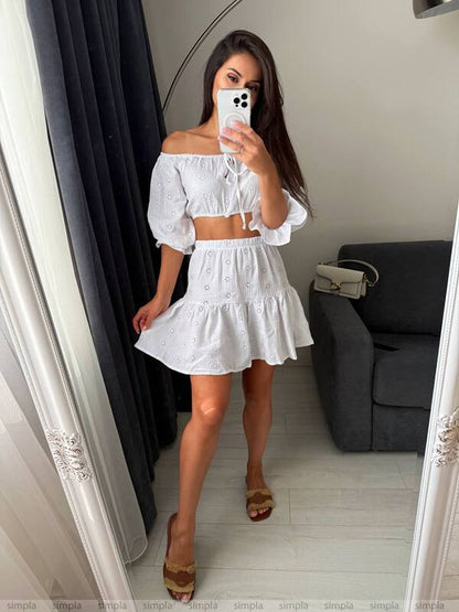 Woman taking a mirror selfie wearing a white off-shoulder top and skirt.