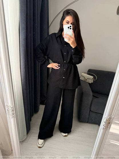 Person wearing a black outfit taking a mirror selfie in a room with a gray sofa.