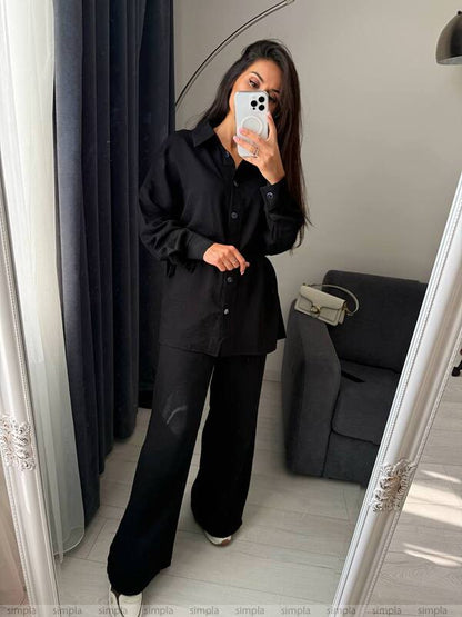 Person taking a mirror selfie wearing a black outfit in a room with a gray sofa.