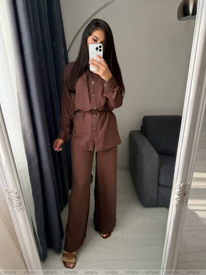 Person wearing a brown outfit taking a mirror selfie in a room with a gray sofa.