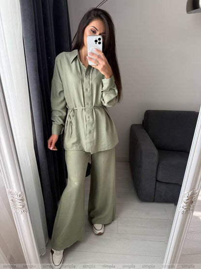 Woman taking a mirror selfie wearing a green outfit in a room with a gray sofa.