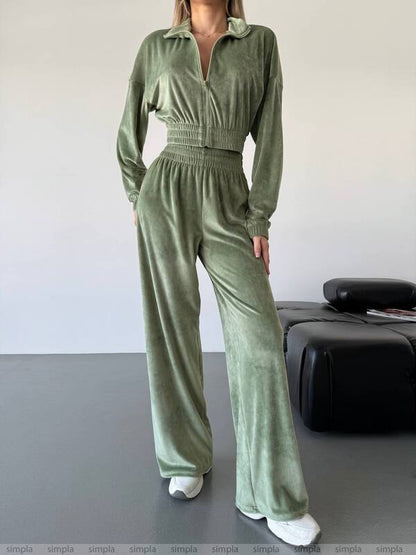 Person wearing a green velvet tracksuit in a minimal indoor setting.