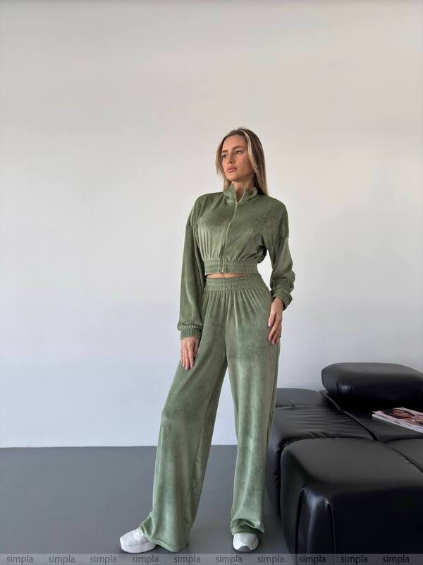 Person wearing a green tracksuit standing in a minimal room with a black couch.