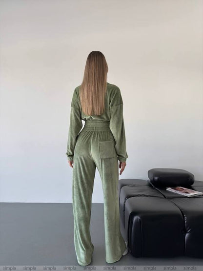 Person wearing a green jumpsuit standing in a minimalistic room with a black sofa and white wall.