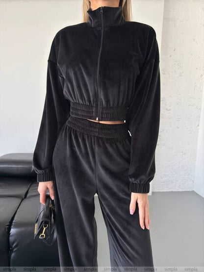 Person wearing a black tracksuit holding a black handbag indoors.