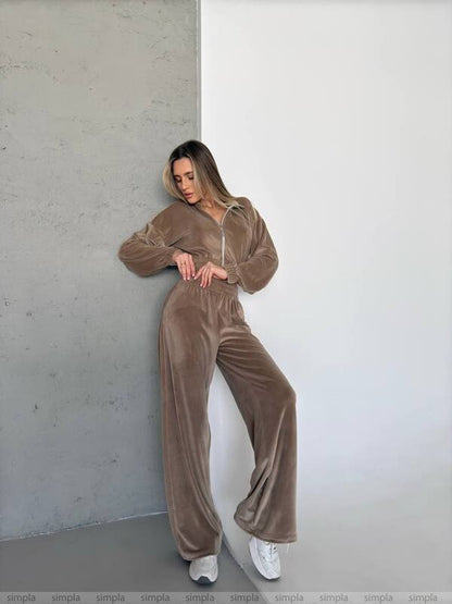 Woman wearing a brown velour tracksuit against a white wall.