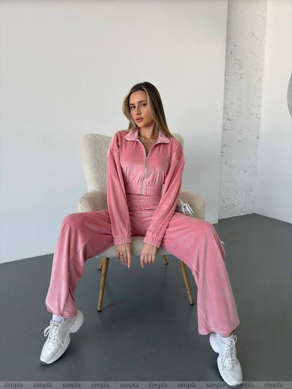 Woman sitting on a chair wearing a pink tracksuit with white sneakers in a minimalistic room.