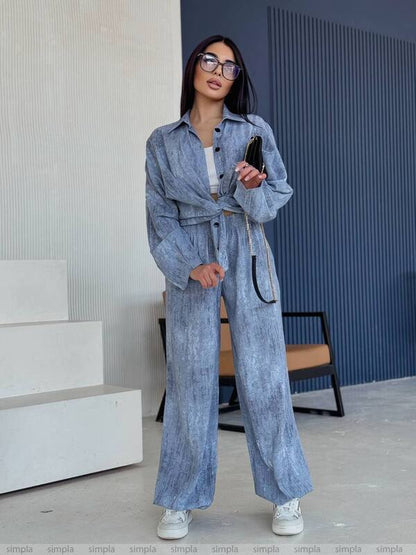 Woman in a blue denim outfit standing indoors with a phone.