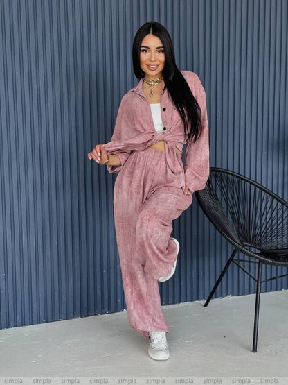 Woman in a pink velvet outfit standing against a blue corrugated metal wall.
