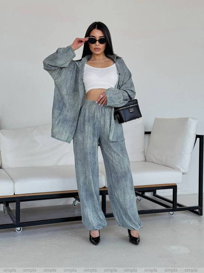 Woman in a gray outfit with a white top and wide-leg pants, standing in a minimalistic room.