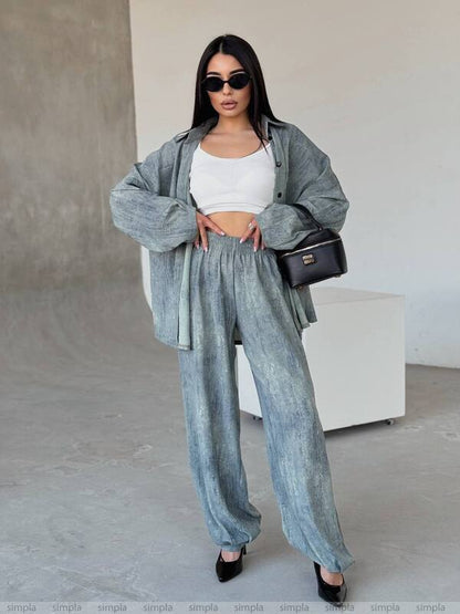 Woman in a stylish outfit with a gray jacket and pants, white top, and black sunglasses, standing against a neutral background.