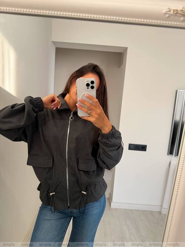 Person wearing a black jacket and blue jeans taking a mirror selfie.