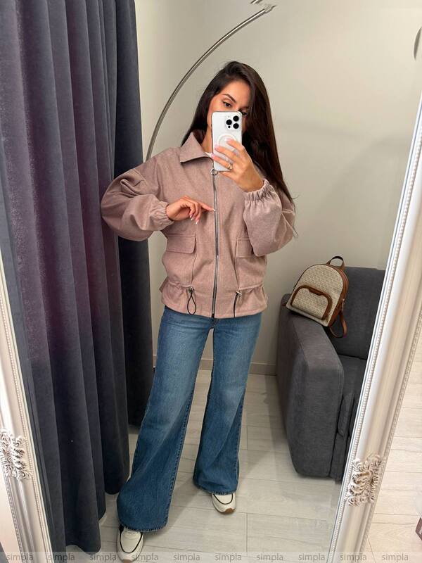 Person wearing a pink jacket and blue jeans taking a mirror selfie.