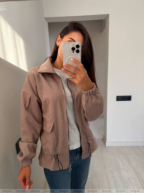 Woman taking a mirror selfie wearing a brown jacket and blue jeans indoors.