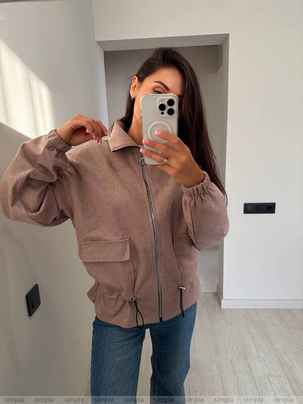 Person wearing a pink jacket taking a mirror selfie in a room.
