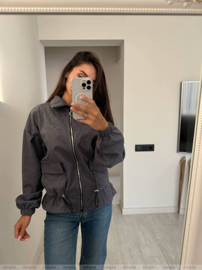 Person wearing a gray jacket and blue jeans taking a mirror selfie.