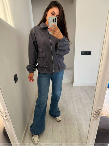 Person wearing a gray jacket and blue jeans taking a mirror selfie.