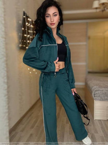 Woman wearing a teal tracksuit holding a black bag indoors.