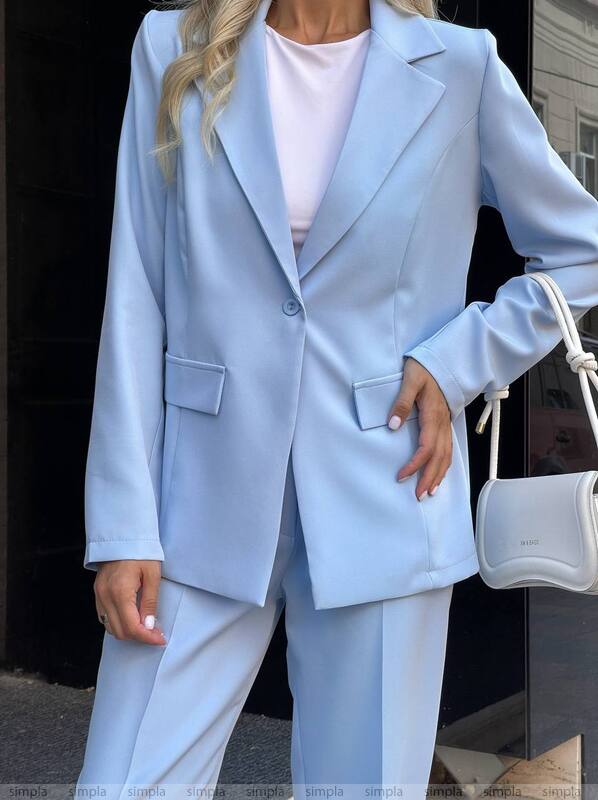 Person wearing a light blue suit with white pants and holding a white handbag.