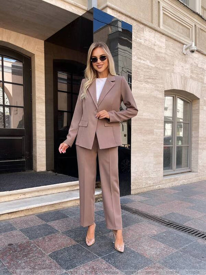 Woman in a beige suit standing in front of a building entrance.