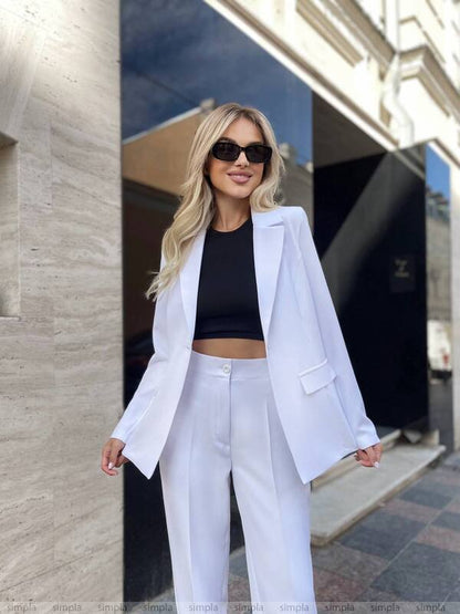 Woman in a white blazer and pants standing outdoors.