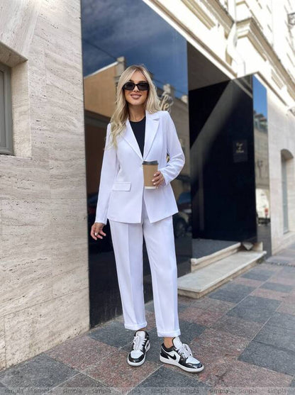 Woman in a white suit standing outside a building holding a coffee cup.