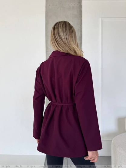 Person wearing a purple coat standing in a minimalistic room.