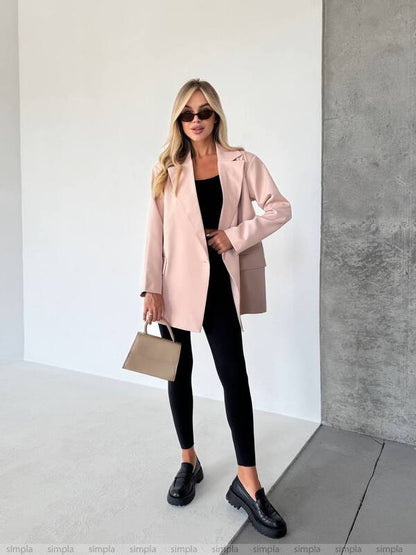 Woman wearing a pink coat, black outfit, and sunglasses indoors.