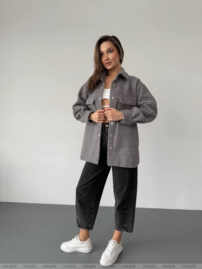 Woman wearing a gray oversized shirt, black pants, and white sneakers on a plain background
