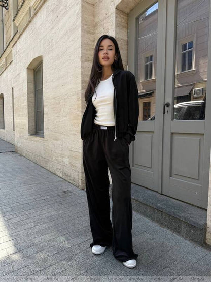 Woman in black outfit standing on a sidewalk with a building in the background