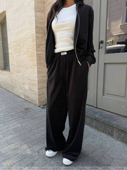 Person wearing a black outfit with a white shirt, standing on a sidewalk.