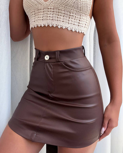 Person wearing a brown leather skirt and beige top against a white background